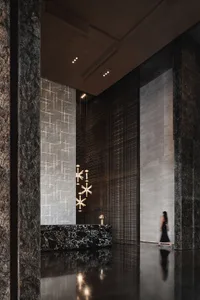 A spacious modern minimalist lobby with marble walls and floors, featuring geometric lighting fixtures and a sleek black rece
