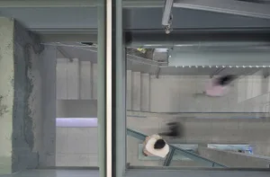 A top-down view of a modern urban concrete and glass walkway with blurred figures indicating movement.