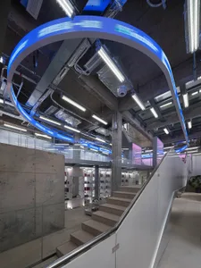 Indoor office space featuring concrete walls, glass walkways, and neon lighting.