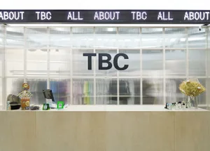 A contemporary reception counter made of wood, featuring a glass partition and a digital message board.