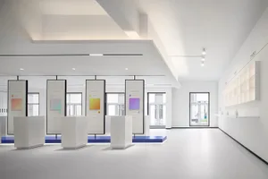 A minimalist space with white walls and floors, featuring art displays on white pedestals and a wall of shelves.