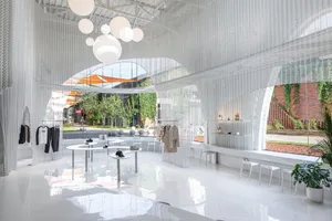 A minimalist clothing store with white interior, metal and glass elements, and potted plants.