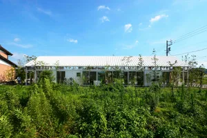 Modern commercial building with metallic roof and walls surrounded by greenery.