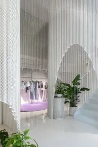 Modern retail store with a white interior, metal perforated screens, and green plants.