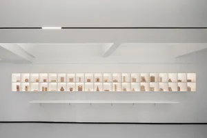 A minimalist art exhibit featuring various paper sculptures displayed on illuminated shelves.