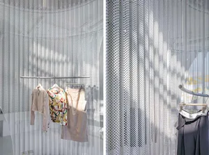 Clothing garments displayed on a rack with a perforated metal barrier in the background.