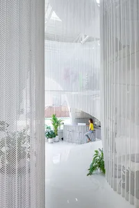 A minimalist office space featuring a metal screen, white flooring, and potted plants.