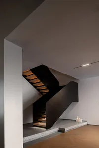 Modern staircase with black handrail and wooden steps illuminated by soft lighting.