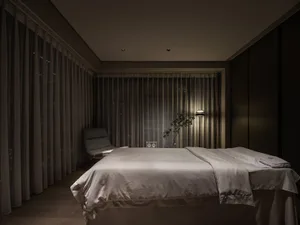 A minimalist bedroom featuring a bed with textured fabric, surrounded by sheer curtains and a floor lamp, creating a serene a