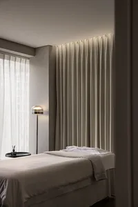A minimalist bedroom featuring soft textiles, a neatly made bed, and a simple, elegant floor lamp.