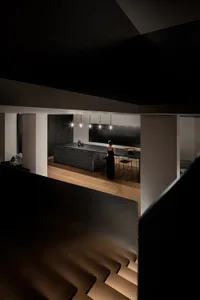A modern black kitchen interior with a minimalistic design, featuring a long kitchen island with pendant lights and a person 