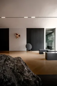 A minimalist living room with wooden floors, black walls, a black round speaker, and stone-like objects.