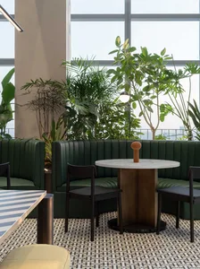 A modern cafe interior featuring green leather seating, marble table tops, and wooden furniture.