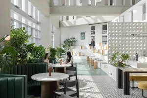 Modern cafe interior with green chairs, round marble tables, and plants.