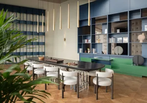 A contemporary dining room featuring a long wooden table surrounded by white chairs with geometric patterns, set against a ba