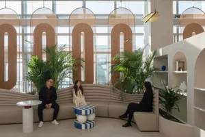 People sitting in a modern office lounge with concrete and fabric seating, glass partitions, and green plants.