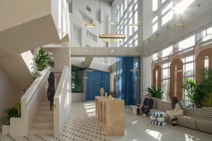 A spacious, modern office space with concrete walls and flooring, featuring minimalist furnishings and large windows.