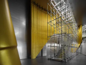 Metal scaffolding structure with yellow metal elements in an industrial interior setting.