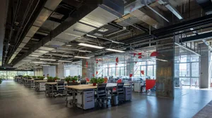 Industrial office space featuring concrete walls and floors, with exposed pipes and large windows.