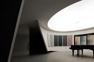 Modern room with minimalist design features a grand piano and color samples on the wall.
