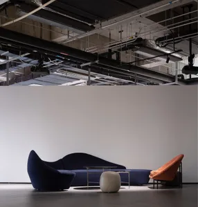 A modern lobby featuring a blue upholstered couch, an orange armchair, and a sleek metallic coffee table in front of a white