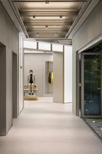 A modern retail space featuring minimalist concrete surfaces, with a mannequin dressed in a beige suit seated on a platform.