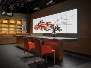 A modern commercial interior space with a concrete desk area featuring orange chairs and a large screen displaying product im