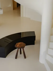 A minimalist room with a black curved bench and wooden stool, featuring modern interior design elements.