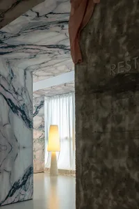 A minimalist interior space featuring marble walls and a concrete pillar.