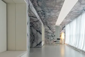 A modern living room with marble walls and ceiling, featuring sleek furniture and a floor-to-ceiling window.