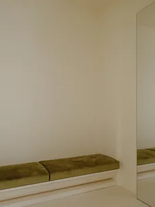 A minimalist interior space featuring a green velvet cushion on a white shelf.