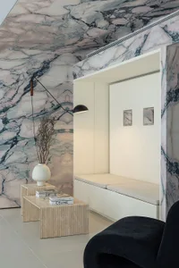 A minimalist living room with marble walls and floor, featuring a built-in seating area, side tables, and a black armchair.