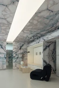A contemporary living area featuring luxurious marble walls and ceiling, with sleek black furniture and minimalist decor.