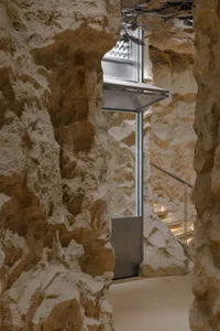 A modern, minimalist concrete reception area with a glass elevator lift and staircase.