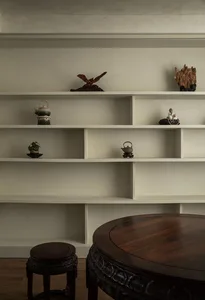 A minimalist living room featuring a white bookshelf with various decorative items and a wooden table.