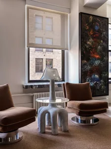 A modern living room with concrete furniture, a glass table centerpiece, and a large abstract painting on the wall.