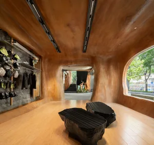 A modern retail storefront with a wooden interior, featuring curved walls, black rock tables, and a view of the outdoors.