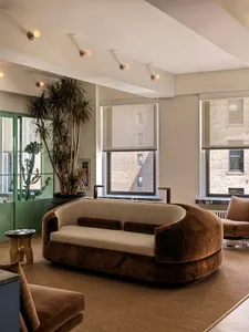 A modern living room featuring a stylish, curved velvet couch with a window view and potted plant.