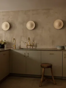 A modern, minimalist residential kitchen featuring concrete countertops and walls, with brass faucets and a stool.
