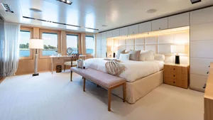 Modern bedroom with a large bed, wooden dresser, and large windows overlooking the sea.