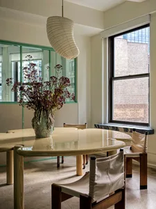 Modern dining room featuring a round glass table surrounded by wooden chairs and a hanging light fixture.