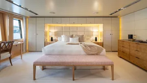 A cozy bedroom with a white bed, wooden furniture, and a view of the water through the window.