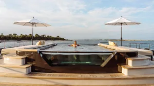 A minimalist glass swimming pool on a yacht with two white umbrellas.