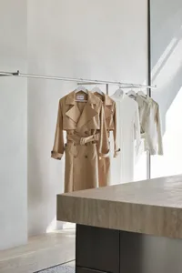 服裝零售展示，展示米色風衣與外套懸掛在金屬衣架上。