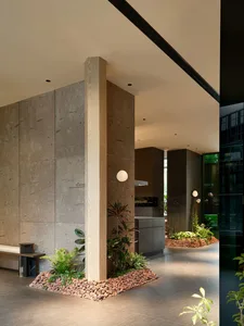 A minimalist modern lobby with concrete walls and flooring, featuring a wooden post and small plant arrangement.