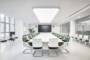 Modern office space with a white table and chairs, green accents, and large windows.