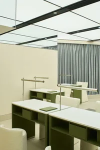 A minimalist school classroom with white walls and furniture, green storage compartments, and metal railings.