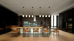 A modern residential kitchen featuring wooden chairs, glass countertops, and stainless steel appliances.