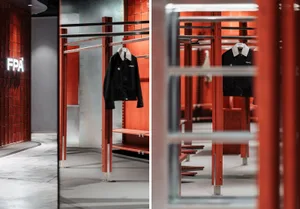 A retail interior featuring red metal racks and wooden shelves displaying clothing items.