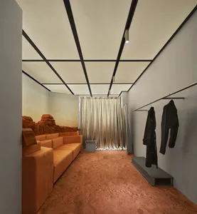 An industrial retail space with concrete walls, glass storefront, and seating area with orange sofas.